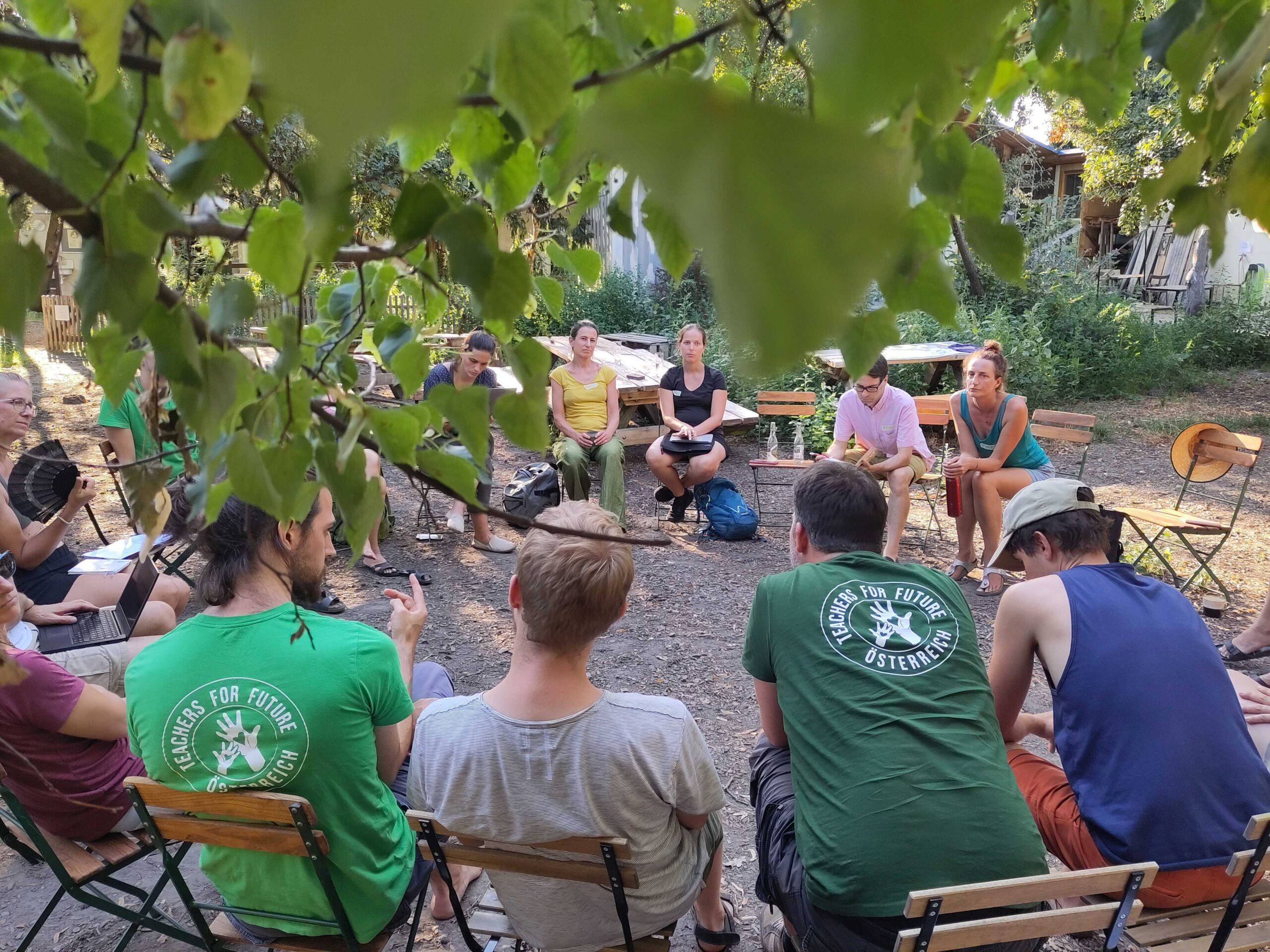 Lehrer*innen sitzen im Sesselkreis und diskutieren unter einem Baum