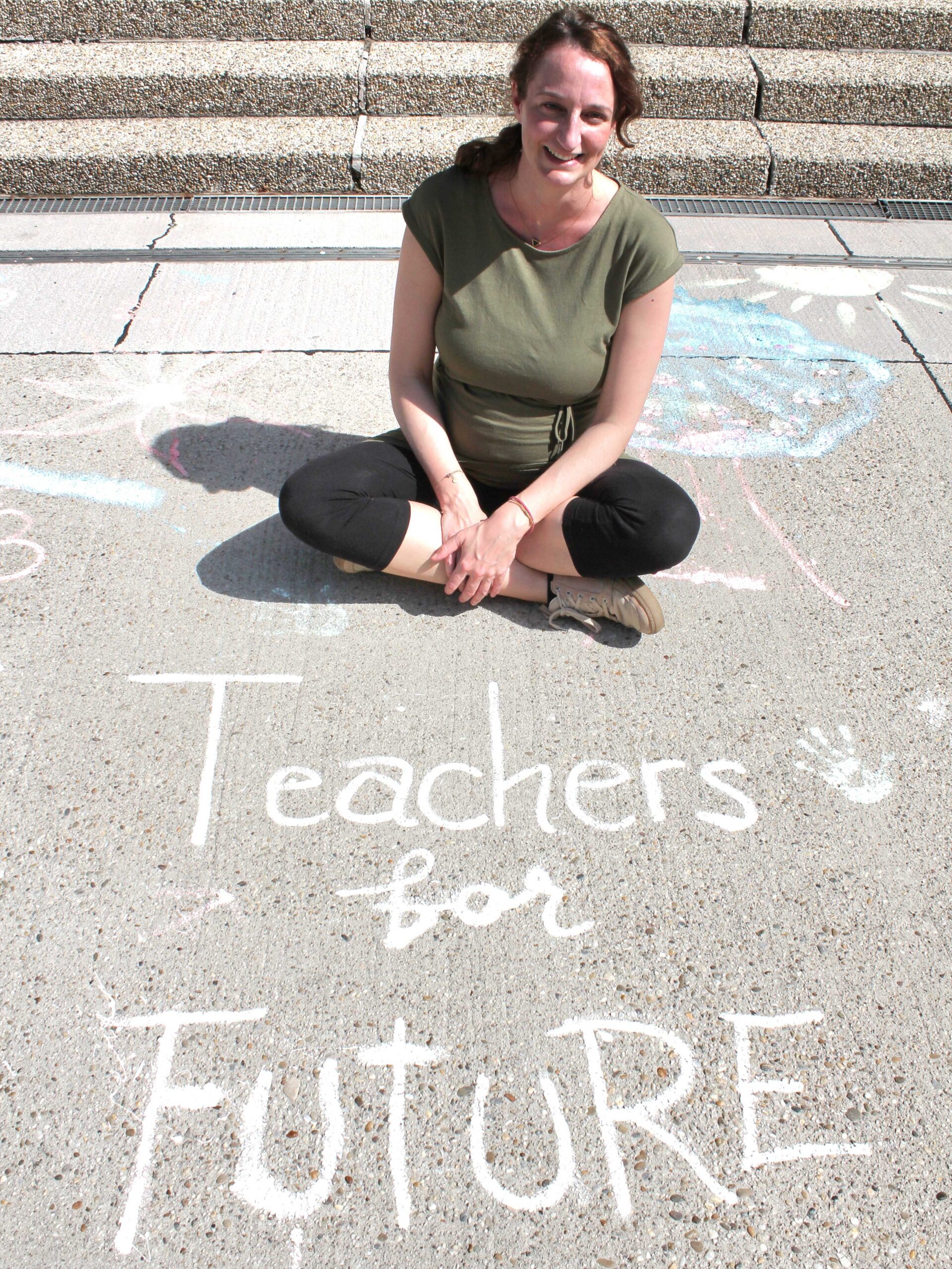 Marietta sitzt auf dem Boden und vor ihr steht mit Straßenkreide geschrieben Teachers For Future.