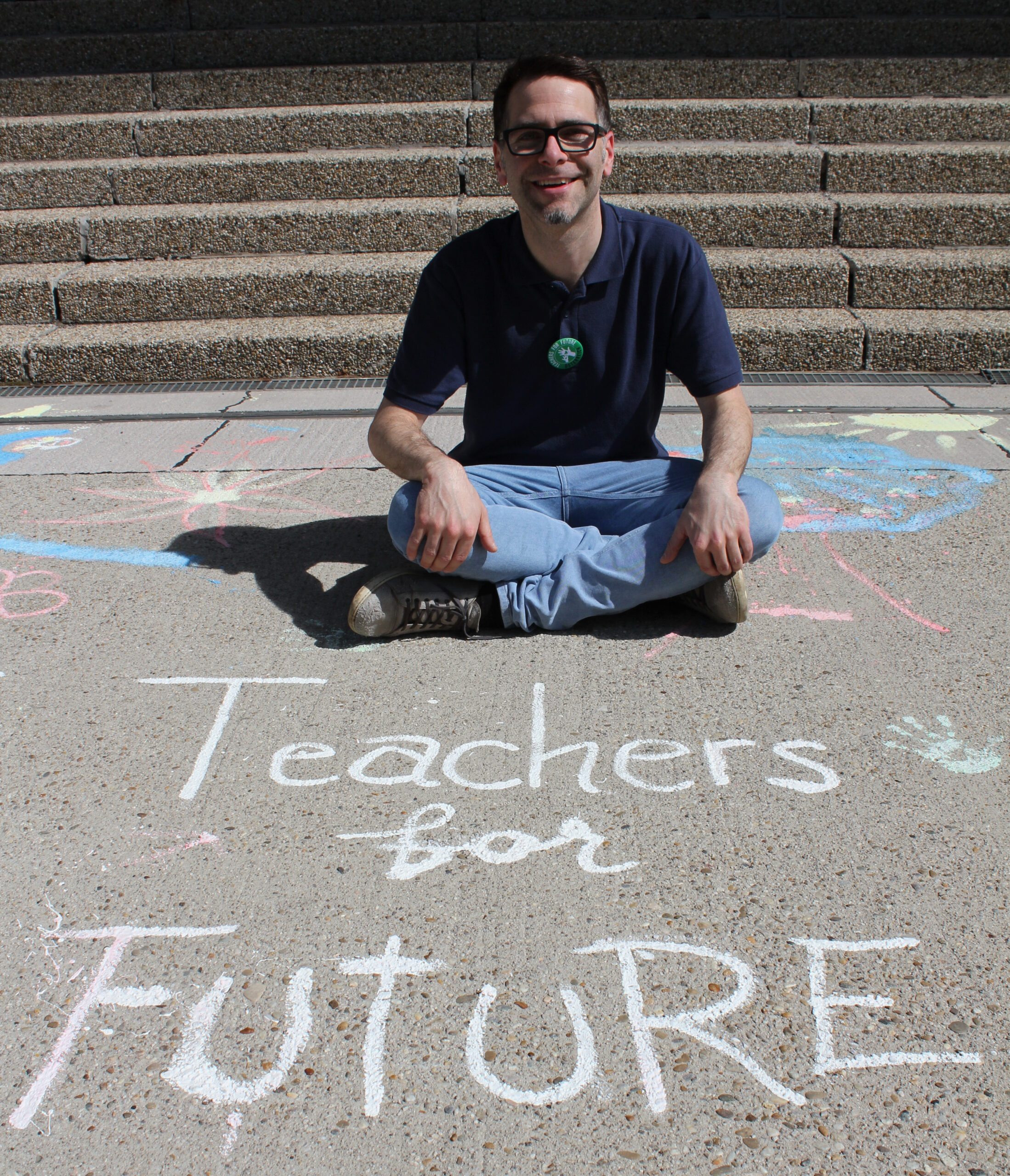 Profilfoto von Reinhard, sitzend vor einem mit Kreide geschriebenen 