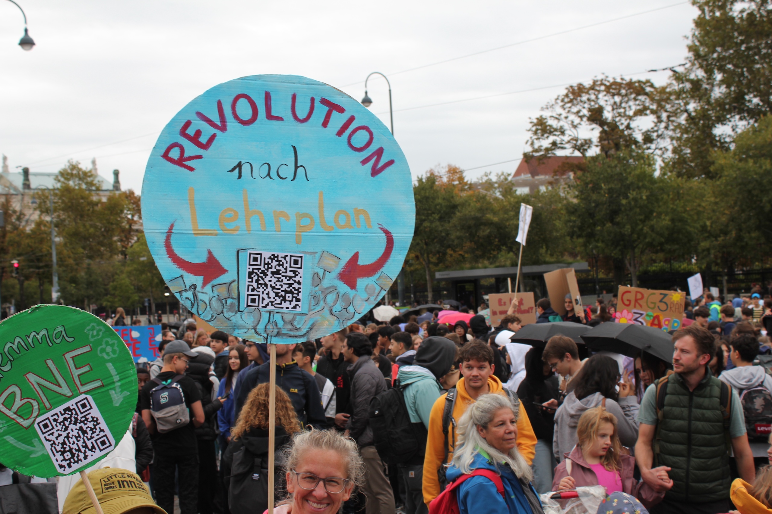 Foto von einer Demonstration. Eine TFF-Aktivistin hält ein Schild mit der Aufschrift "Revlution nach Lehrplan" hoch