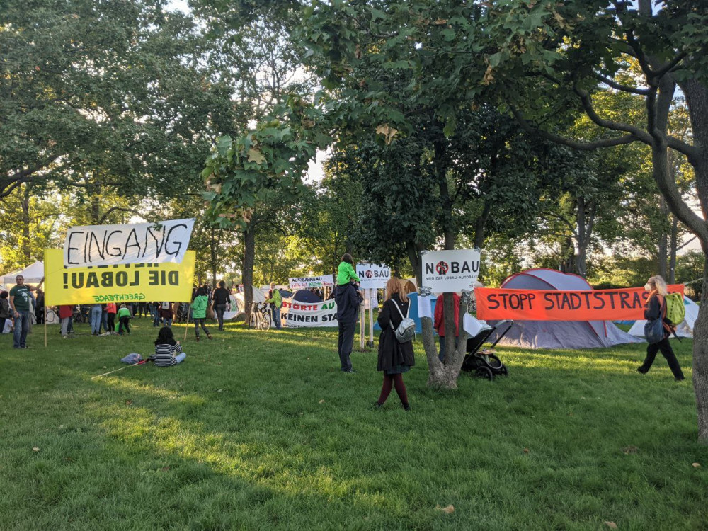 Grüner Park mit diversen, bunten Protestschildern und einzelnen Zelten